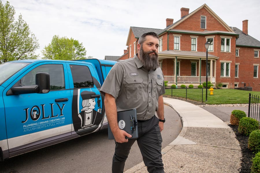 Jolly Plumbing technician walking into appointment with a clipboard.