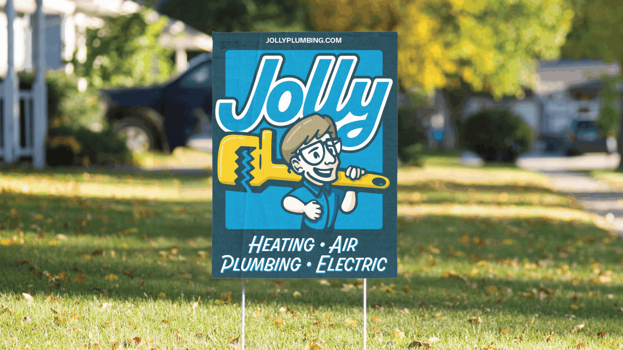 Blue advertising sign in a front yard promoting Jolly with a cartoon technician holding a yellow tool, residential street in background.