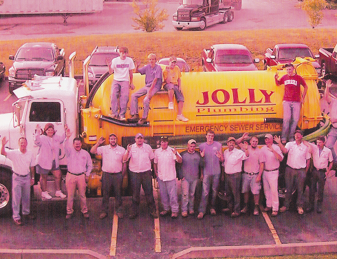 Group of plumbers posing in front of a large yellow sewer truck labeled 'JOLLY PLUMBING' in a parking lot.