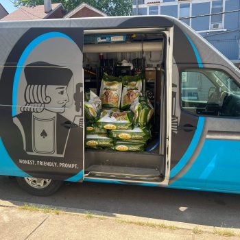 Open side of a blue delivery van filled with bags of groceries; door features a cartoon figure and the slogan 'Honest. Friendly. Prompt.'