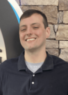 Smiling man in a dark polo shirt stands in front of a stone wall backdrop.