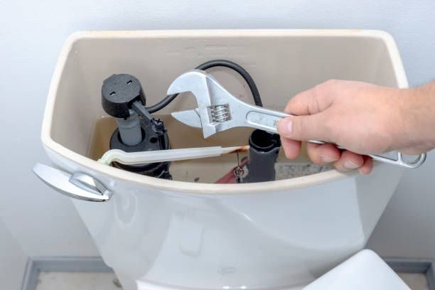 Repairs being completed on a toilet with wrench.