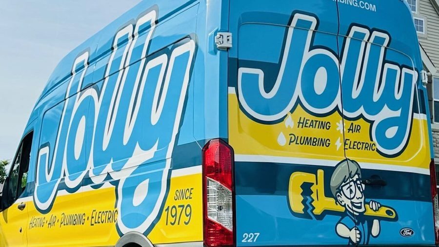 Blue Jiffy service van with large white script 'Jiffy' on a yellow stripe, advertising heating, air, plumbing, and electric; cartoon worker with a wrench on the rear.