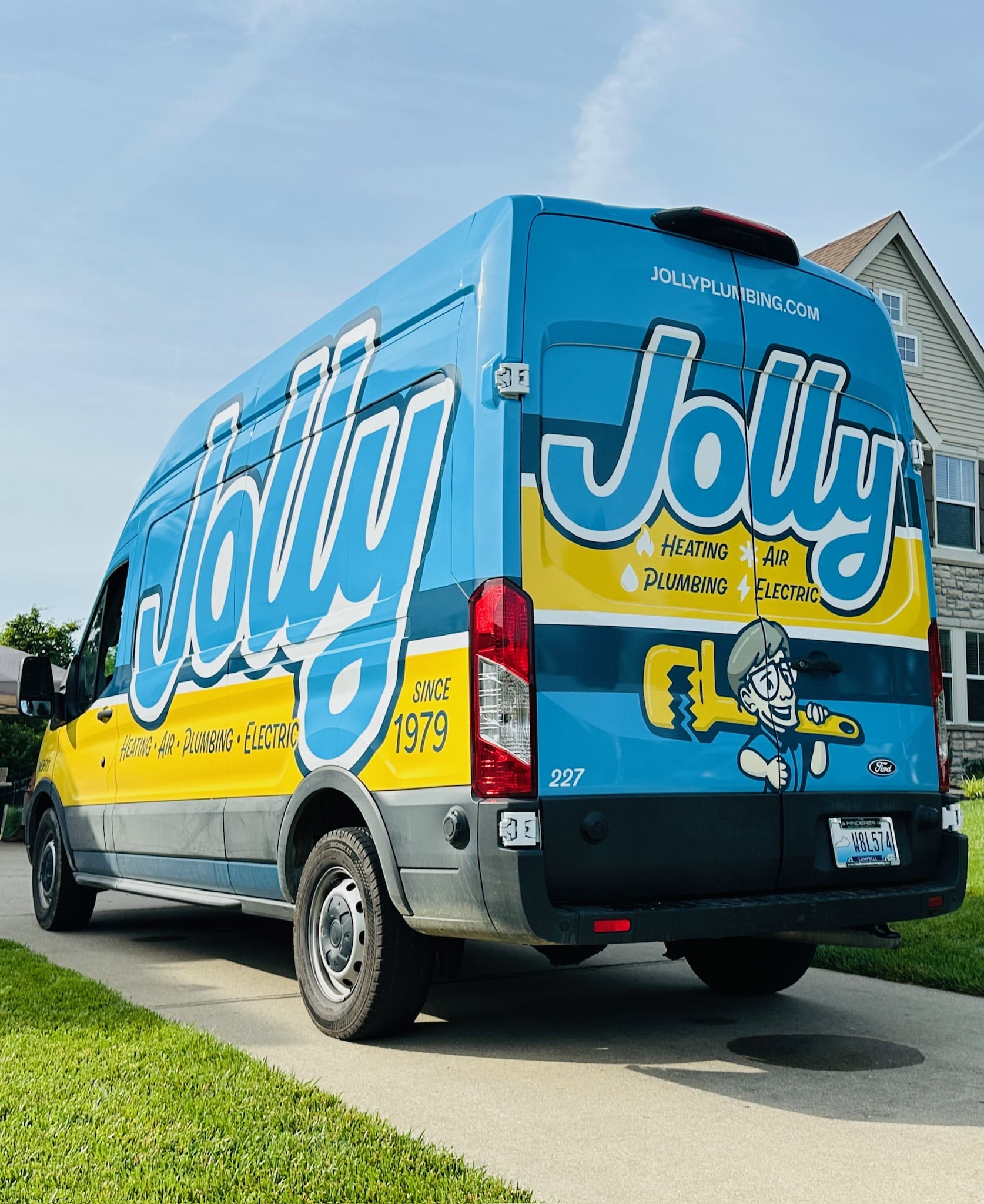Blue Jolly Plumbing service van parked in a suburban driveway, showing company branding and list of services (heating, air, plumbing, electric).