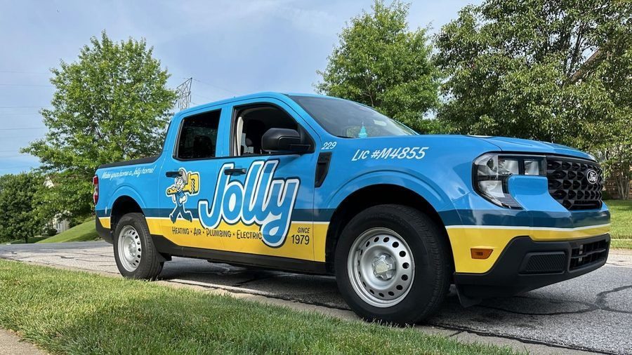 Blue Jolly service truck with yellow stripe parked on a street, advertising heating, air, plumbing, and electric services since 1979.