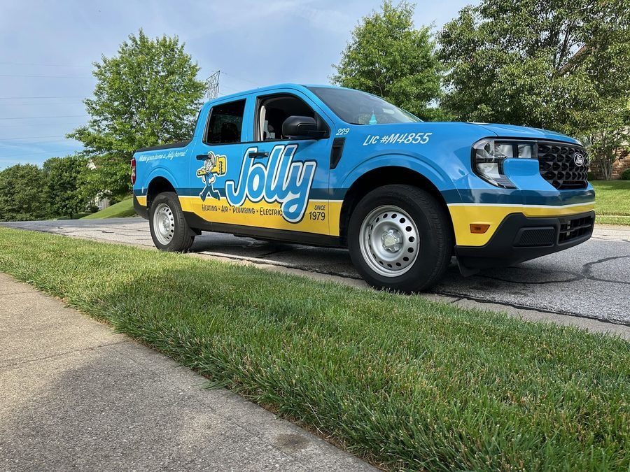 Blue Jolly service pickup with yellow stripe advertising heating, air, plumbing, and electric services parked on a suburban street.